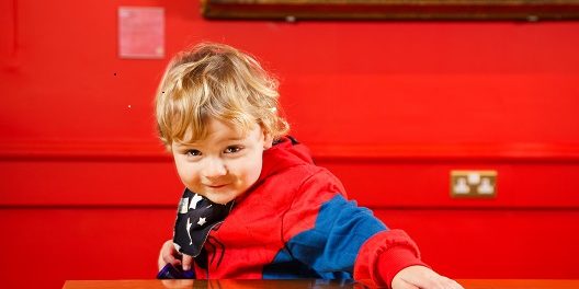 Moonbeams Smiling early years aged boy in a red top, in an art gallery with red walls