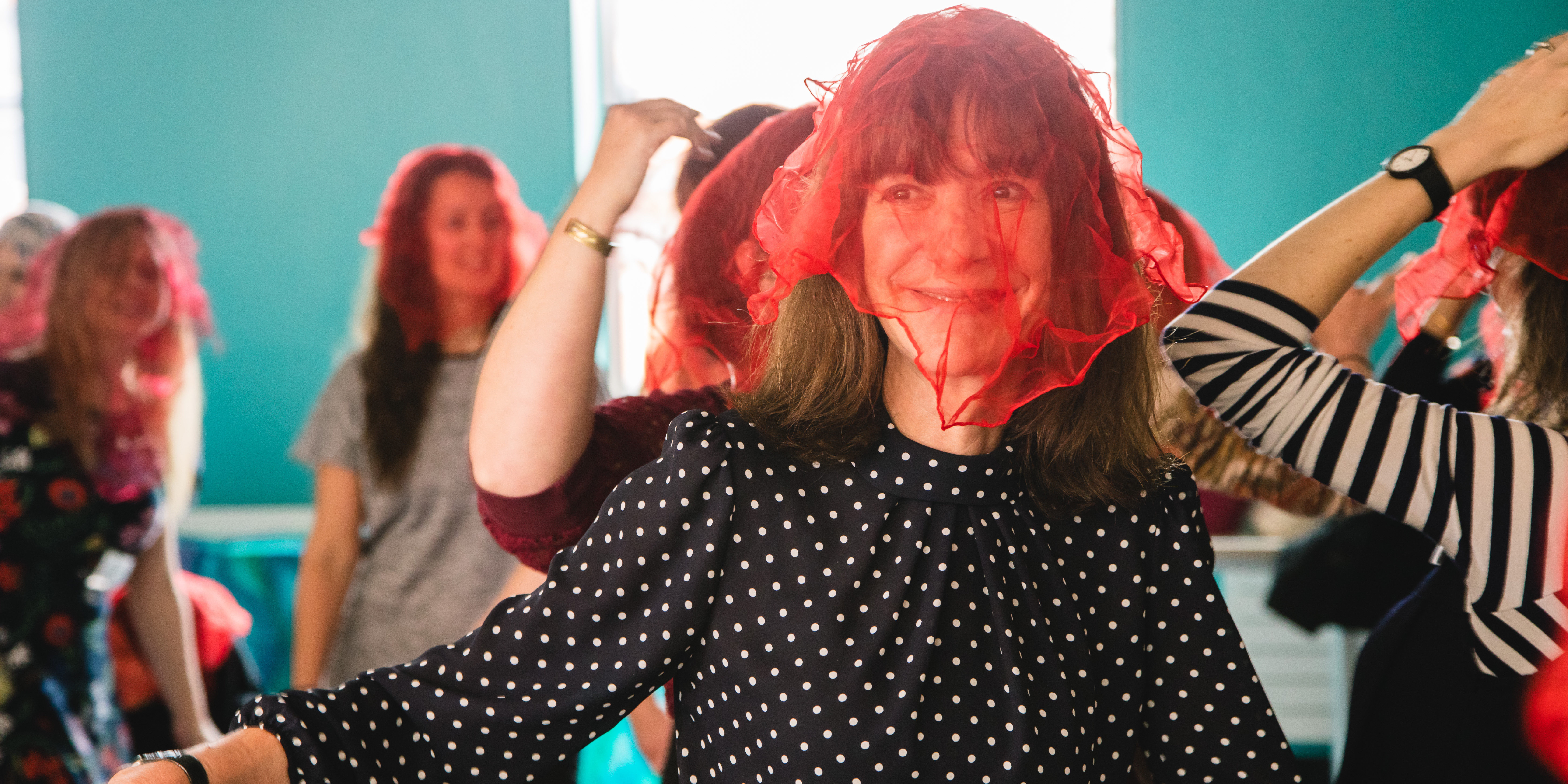 A smiling woman dances with a red scarf on her head