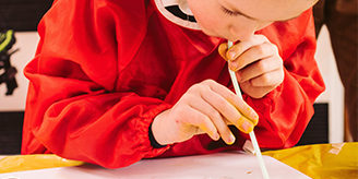 Primary aged boy in an art smock blows paint with a straw onto paper