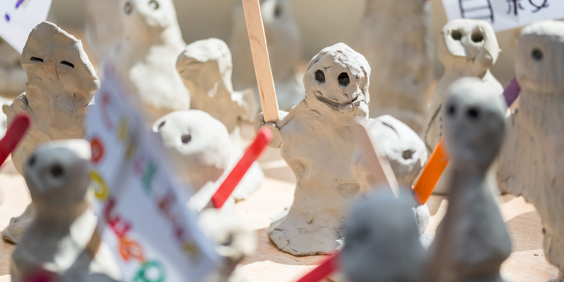 Small grey human like clay figures holding signs