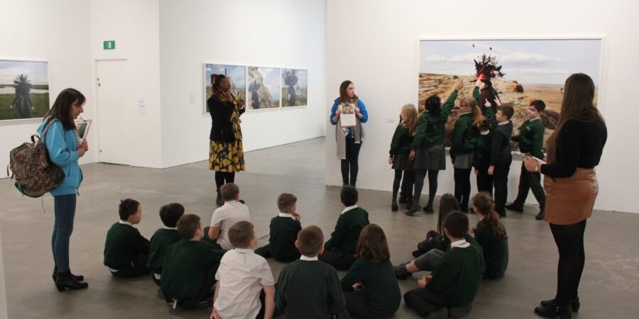 Hob-Green-1-Large-900×600 A group of school children look at art in the Ikon gallery, some are seated and some stand and point at a large image