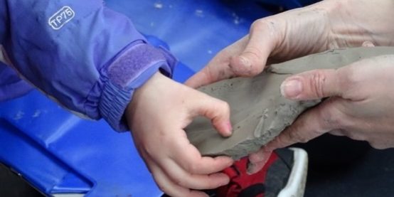 Hands of an adult and young child holding wet clay