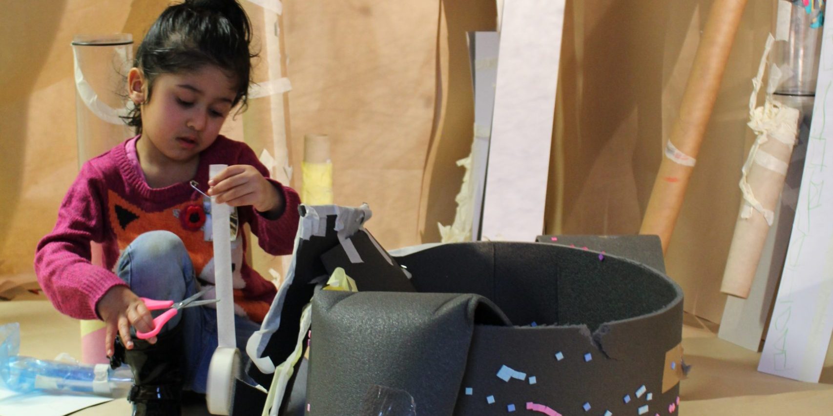 Lilian di Lissa IAleeza constructing her castle Early years child uses scissors to create an artwork. In front of her is a large black structure that she is making